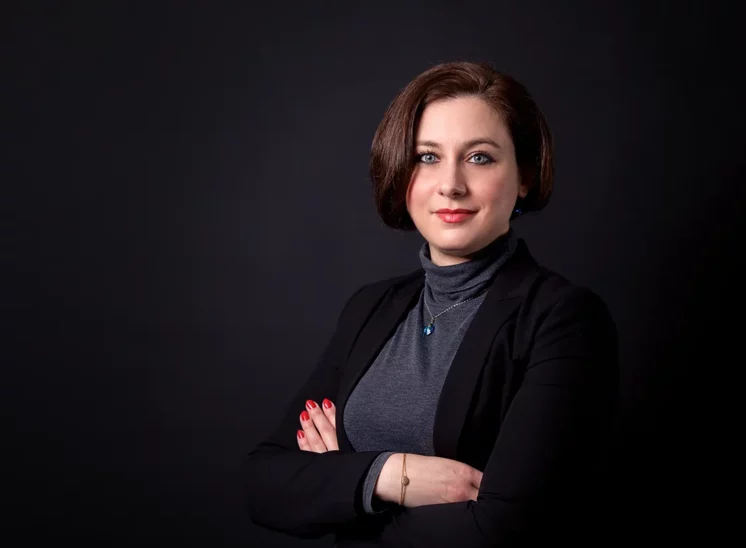 Une femme aux cheveux bruns courts se tient debout sur un fond sombre, incarnant lessence de lélégance dentreprise. Vêtue dun blazer noir et dun col roulé gris, ses bras sont croisés avec assurance avec du vernis à ongles rouge, parfaitement capturé par un photographe qualifié en Seine-et-Marne.
