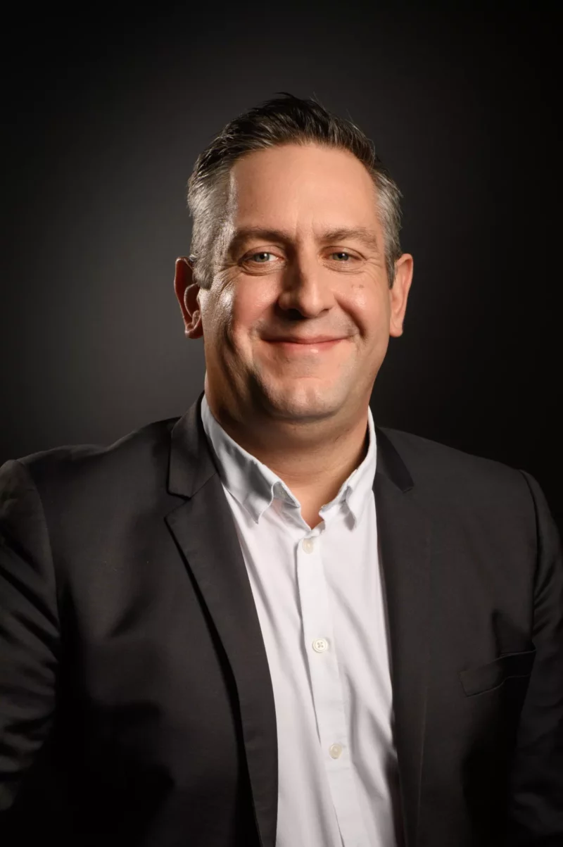Un homme souriant, vêtu dun blazer noir et dune chemise blanche, pose avec assurance sur un fond sombre, incarnant lessence de lélégance dentreprise. Capturée par un photographe talentueux de Seine-et-Marne, cette image reflète le professionnalisme et le charme.
