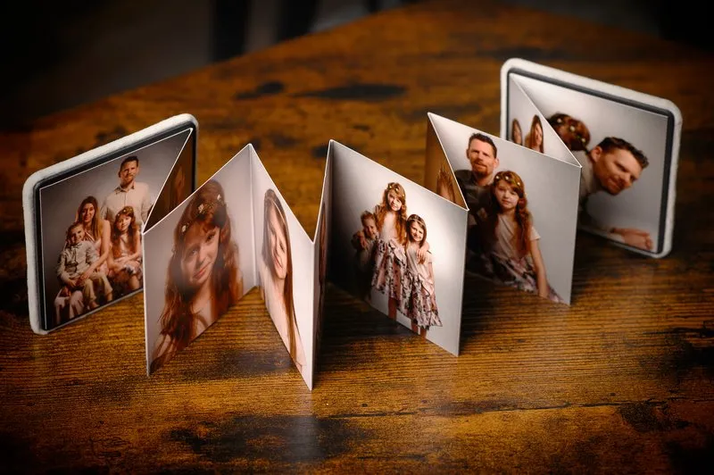 Une table en bois au cœur de la Seine-et-Marne (77) avec une exposition photo en zigzag de portraits de famille. Les images comprennent des photos de groupe et des portraits individuels, le tout dans un style soft focus, avec des tons terreux et une atmosphère chaleureuse.